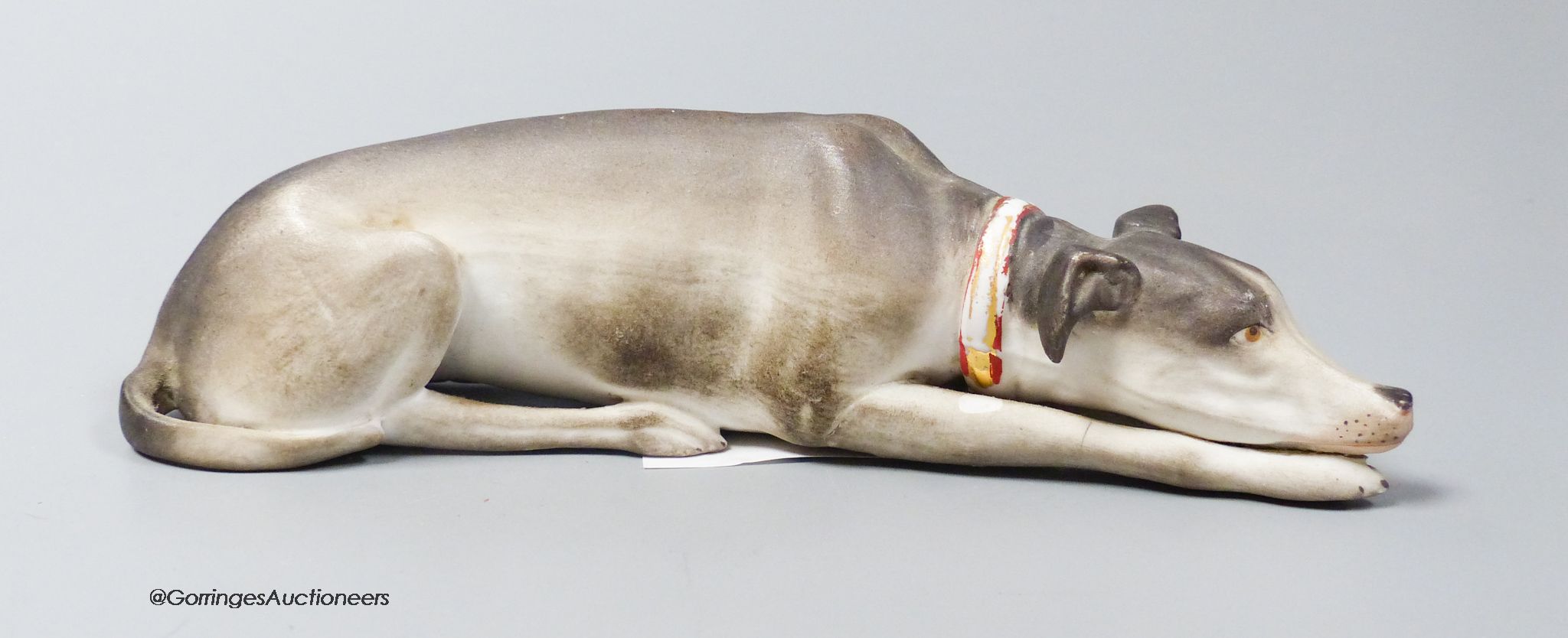 A Continental bisque reclining dog, 17cm